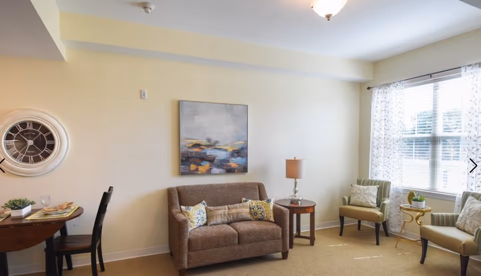Bright living room with a sofa, two armchairs, side tables, wall art and a window with patterned curtains.