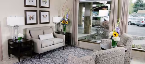 A cozy lounge area with sofa, chairs, lamps, and floral arrangements near windows.