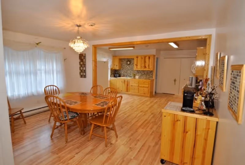 Open dining room with round wooden table, six chairs, and a visible kitchen in back