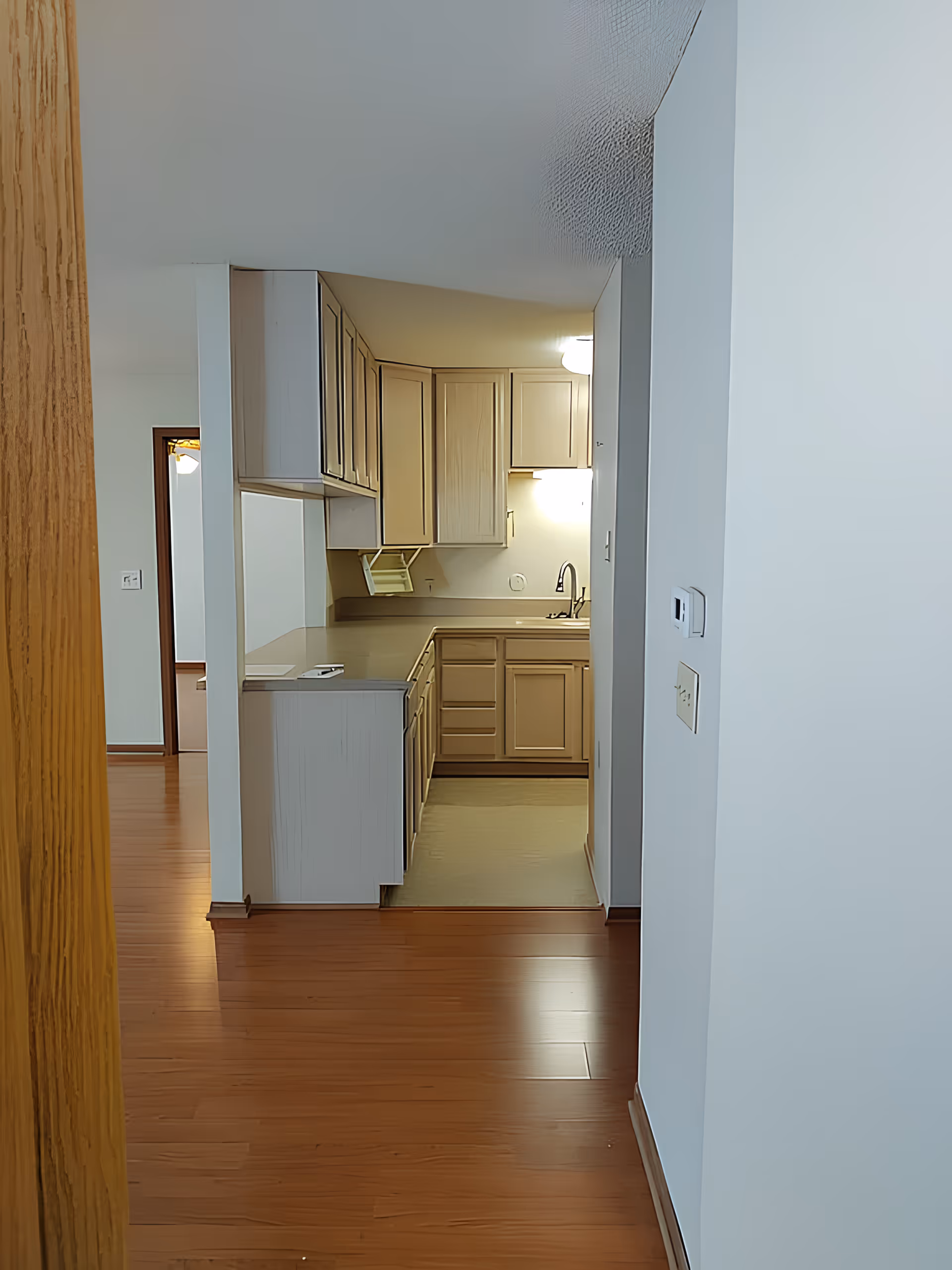 View down a hallway into a small kitchen with wood cabinets, a sink, and hardwood floors.