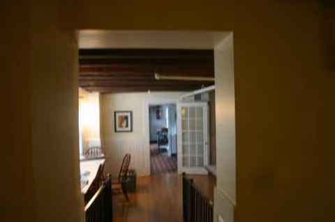 Dim interior hallway opening to a living area with chairs and glass doors.