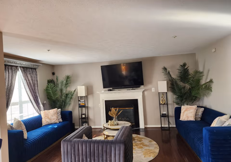 A modern senior living room with blue sofas, a fireplace, and greenery.