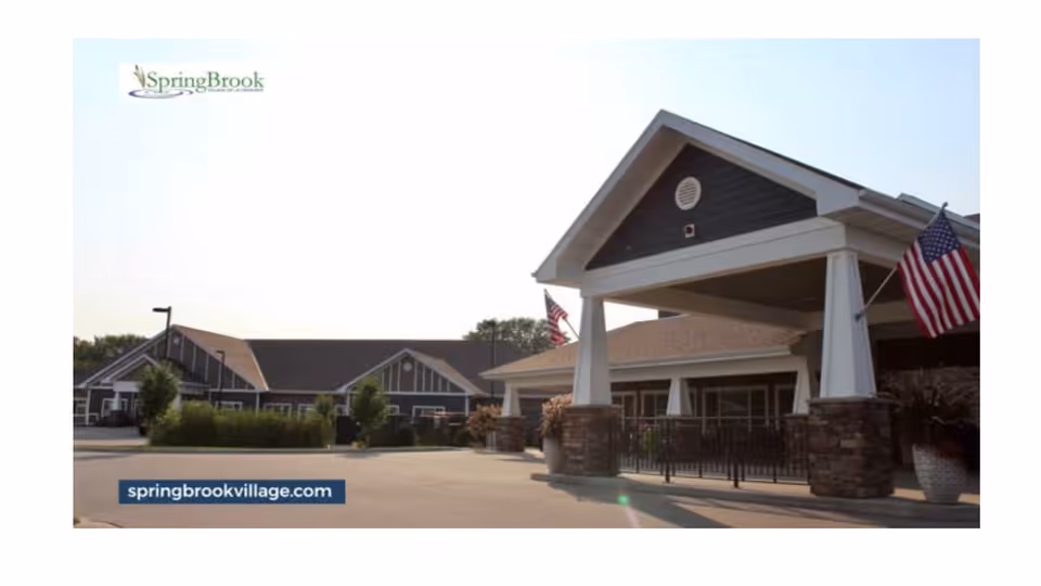 Exterior front entrance of a senior living building with a covered drive-through, American flags, and SpringBrook signage.