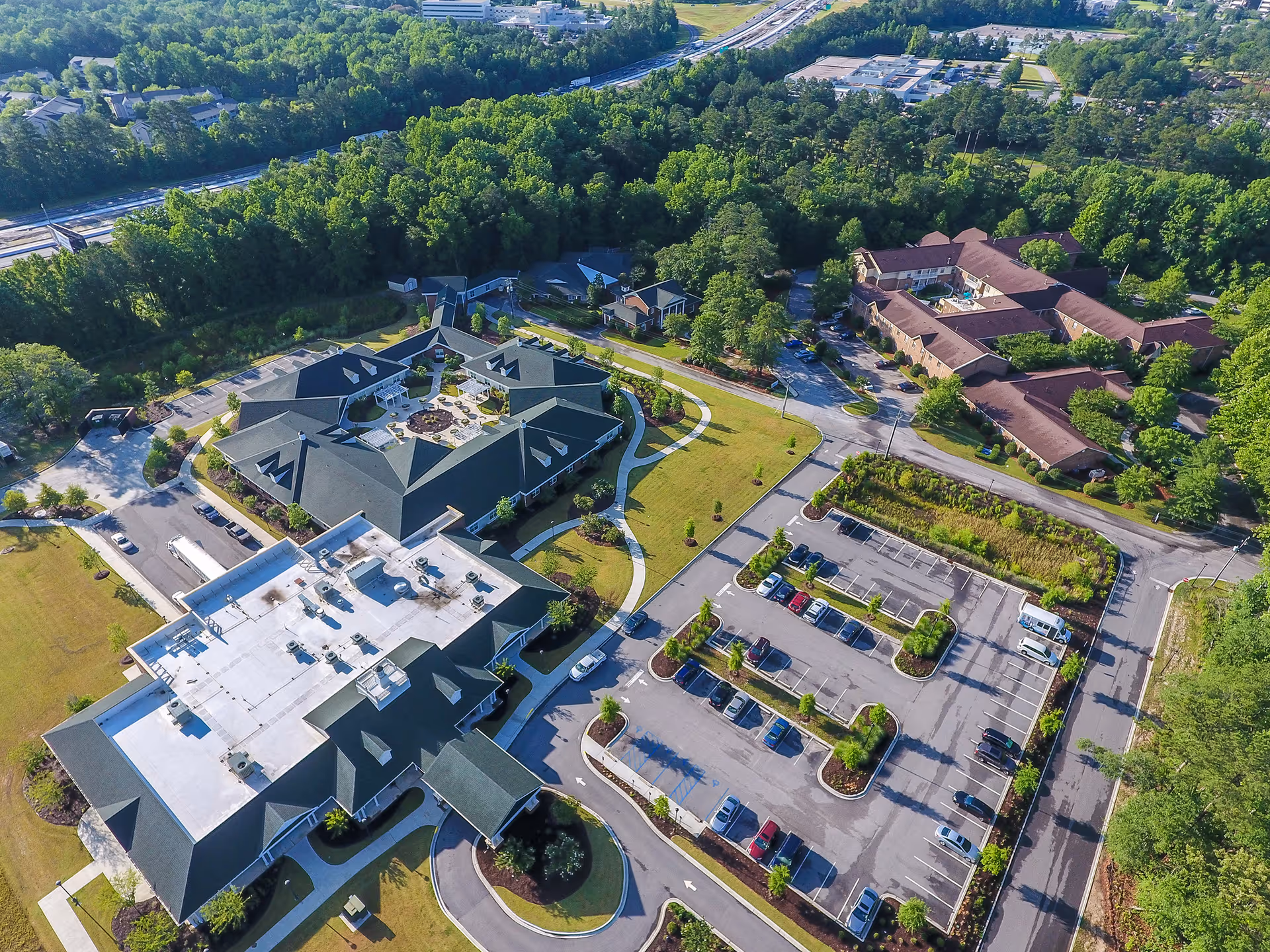 Aerial view of Rice Estate showing multiple connected senior living buildings, a central courtyard, parking lots, driveways, and surrounding trees.