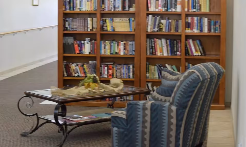 A patterned armchair and glass-top coffee table in front of a wooden bookshelf in a lounge area.
