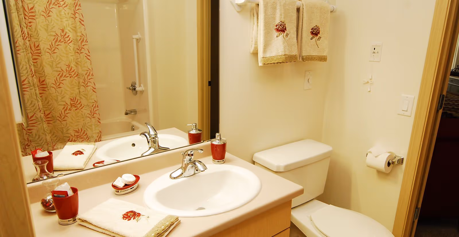 Small bathroom with a sink and vanity, toilet, mirror, and a floral shower curtain with matching towels and accessories.