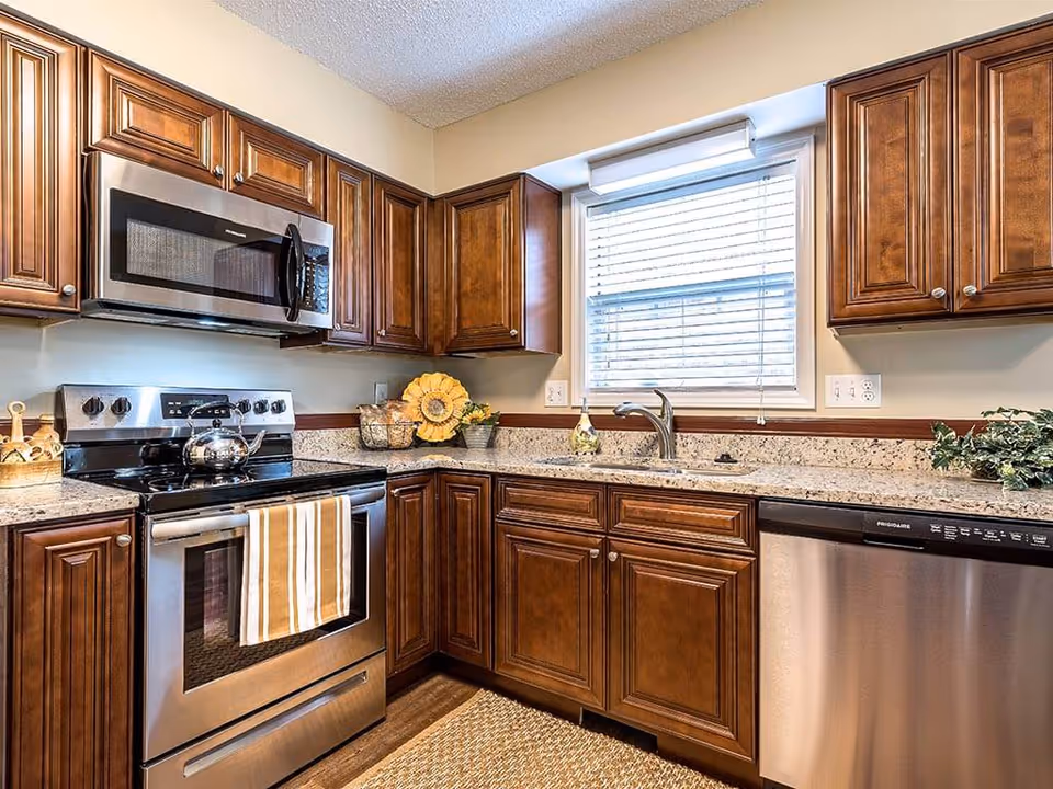 A modern kitchen with wooden cabinets, stainless steel appliances, granite countertops, and a window above the sink.