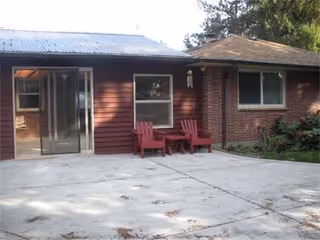 Exterior view of a brick facility with red chairs on a concrete patio.