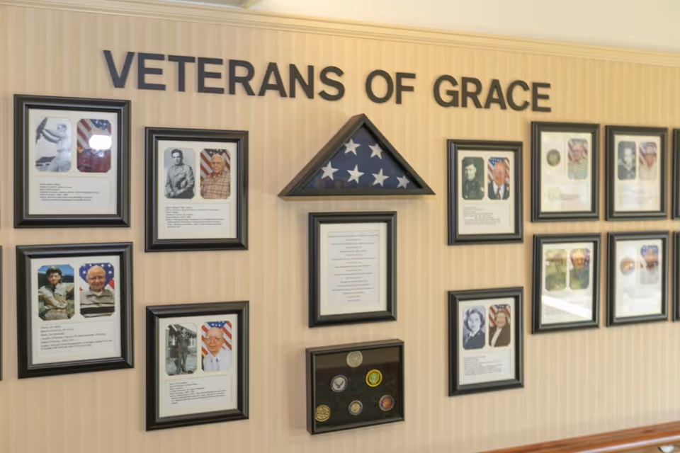 A wall display titled 'Veterans of Grace' featuring framed photographs and biographies of veterans, a folded American flag in a triangular frame, and a display case with military service medals and insignias.