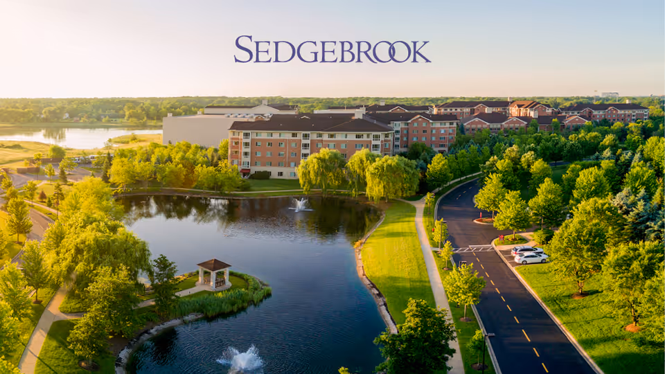 Aerial view of the Sedgebrook senior living campus with a pond, gazebo, walking paths, and multi-story residential buildings.
