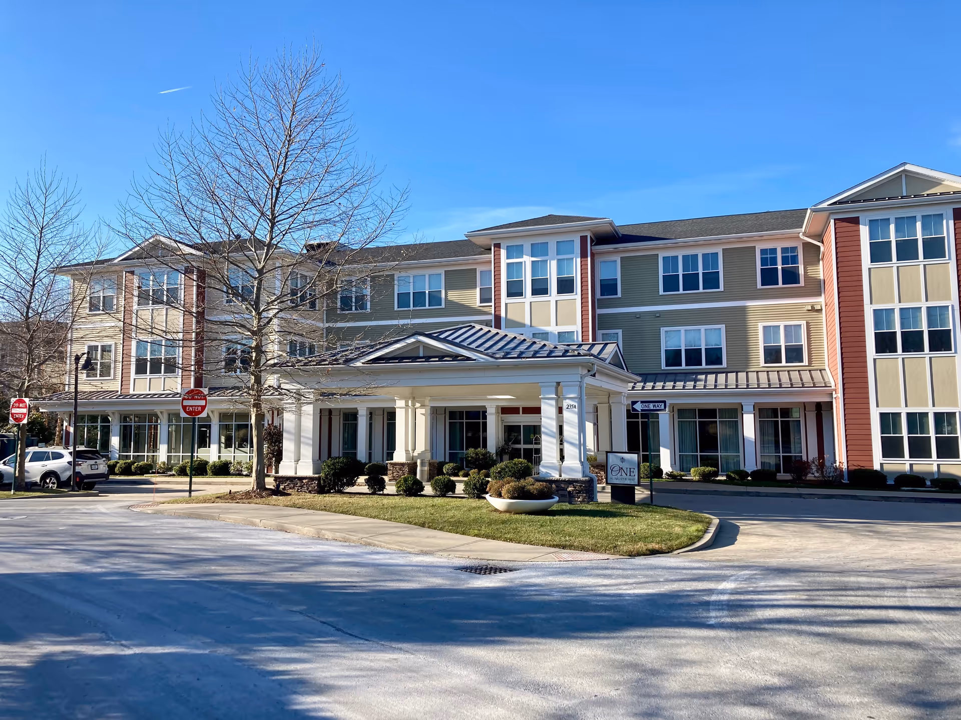 Front exterior of a three-story senior living building with a covered entrance, driveway, and landscaped lawn.