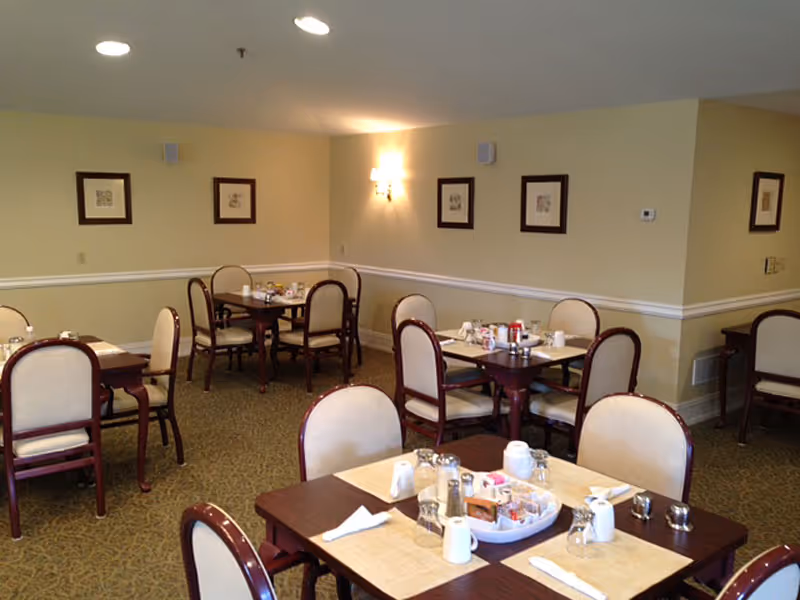 Dining room with several wooden tables and upholstered chairs set for meals.