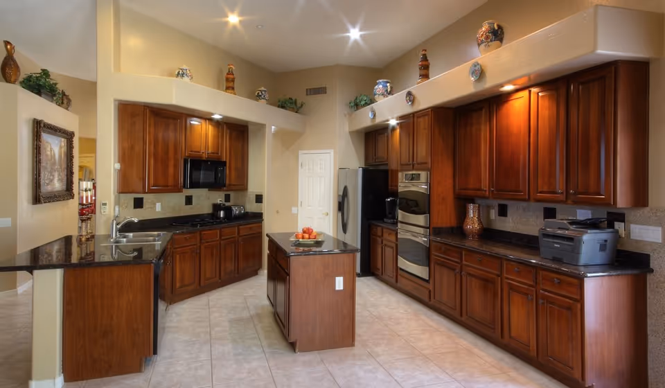 Bright, spacious kitchen with dark wood cabinets, a central island, stainless steel appliances, and tiled floor.