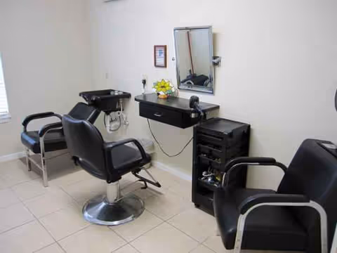 A hair salon inside a senior facility with chairs, mirror, sink, and cart.