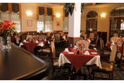 Warmly lit dining room with tables set with red and white tablecloths, chairs, and floral centerpieces.