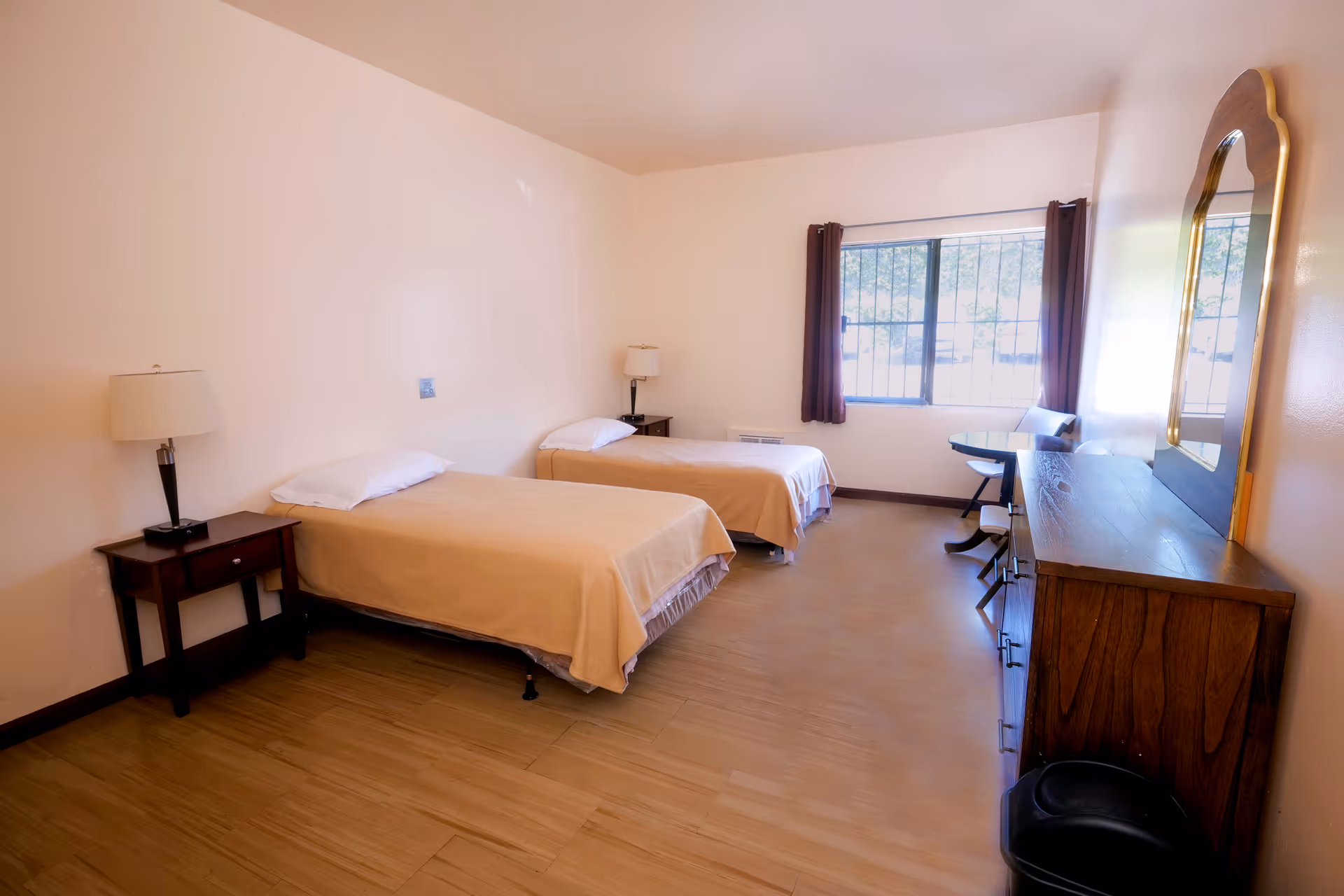 Simple room with two single beds, nightstands, a dresser with mirror, and a window with curtains.