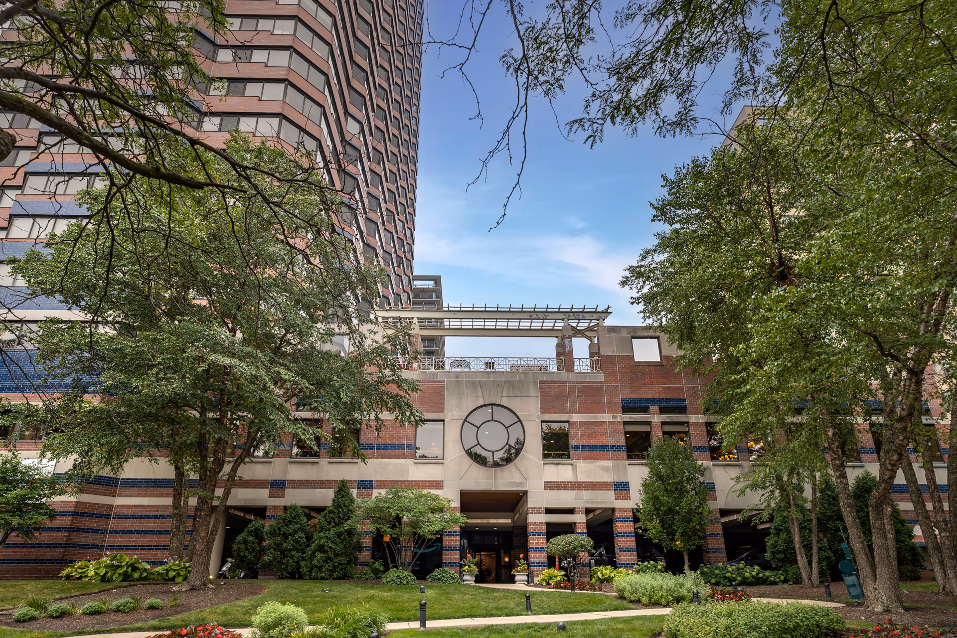 Front exterior of a multi-story brick senior living building with trees and landscaped entrance.