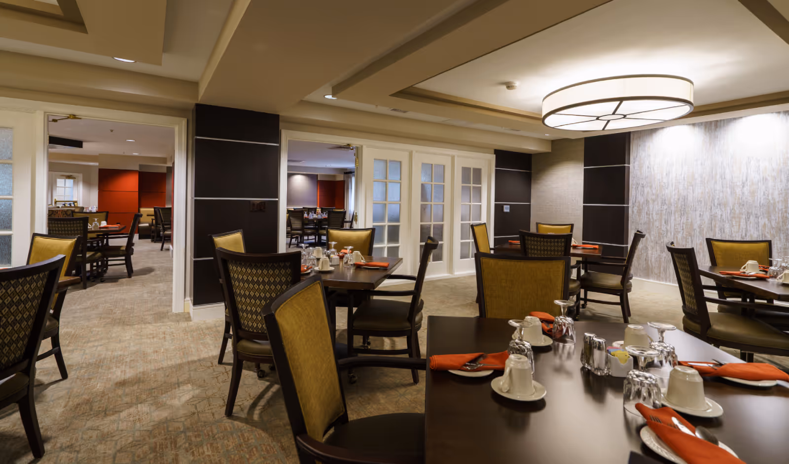Well-lit dining room with multiple set tables and chairs in a senior living community.