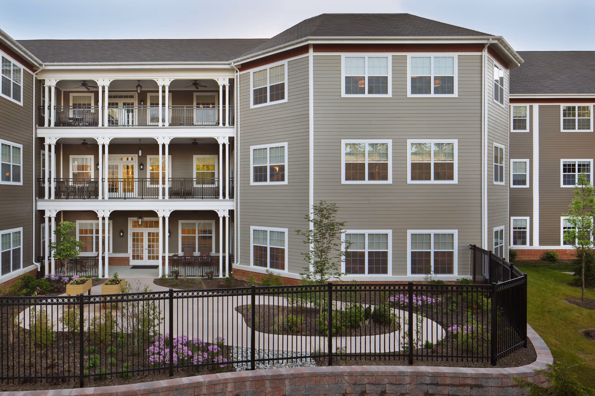 Three-story residential building with covered balconies overlooking a landscaped fenced courtyard.