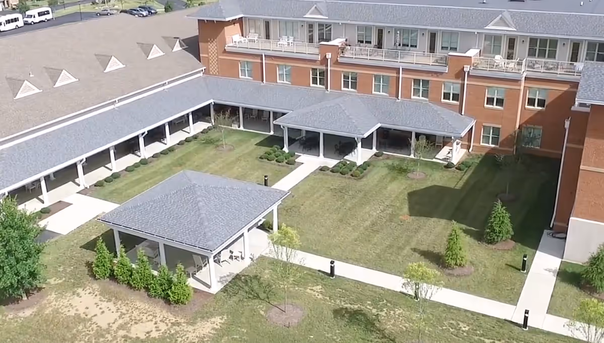 Aerial view of a senior living facility courtyard with covered walkways, two pavilion gazebos, lawns and a multi-story brick building.