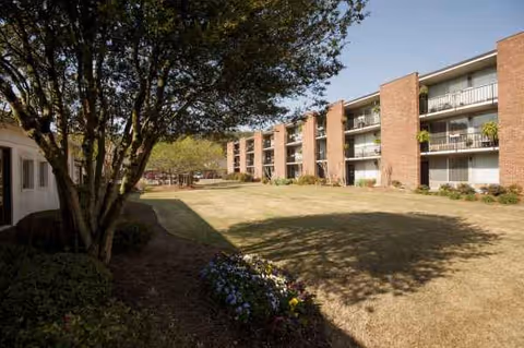 Exterior view of Winthrop Court senior living complex with lawn, trees, and balconies.
