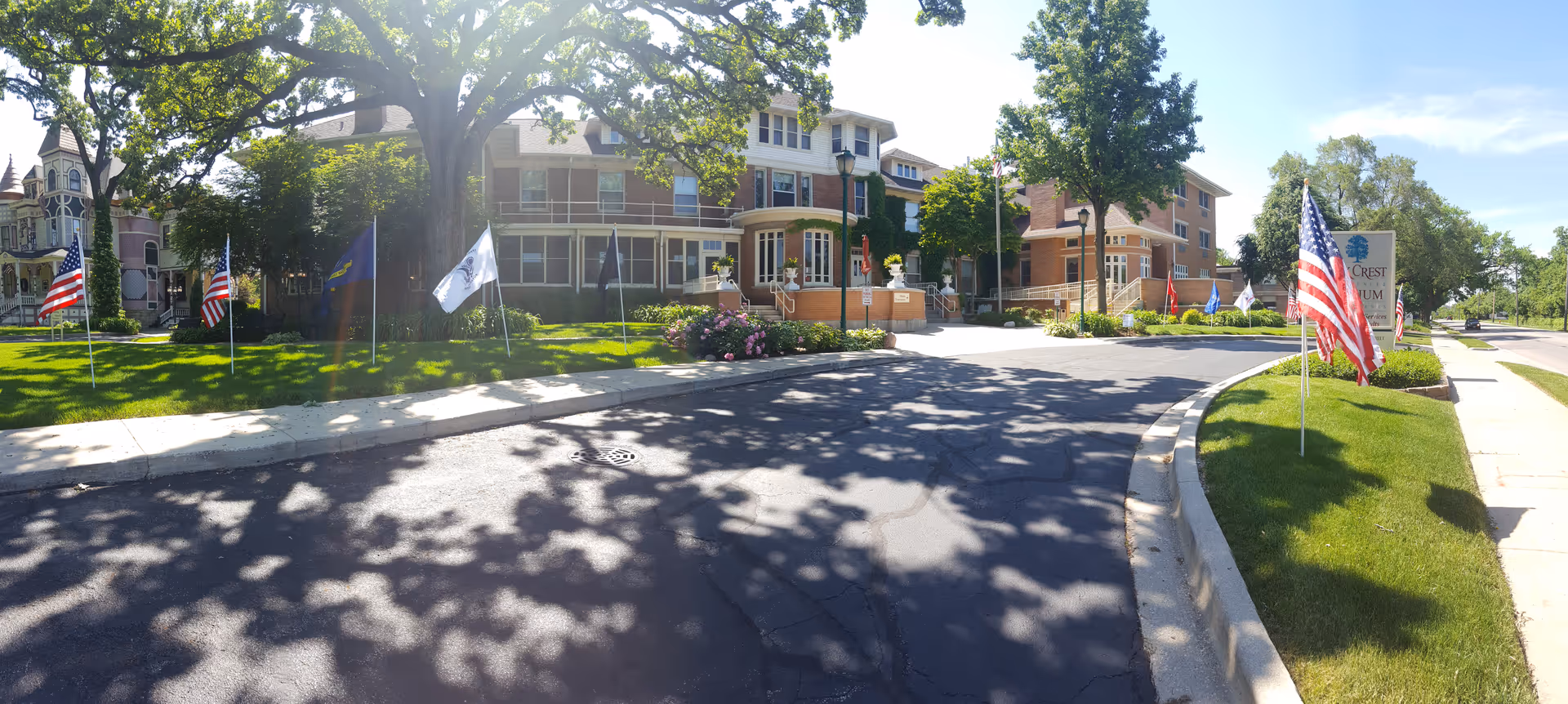 Exterior of Oak Crest Residence & Atrium Apartments with flags along a curved driveway.