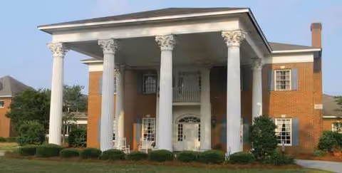 Brick senior living building with a grand columned entrance and manicured shrubs.