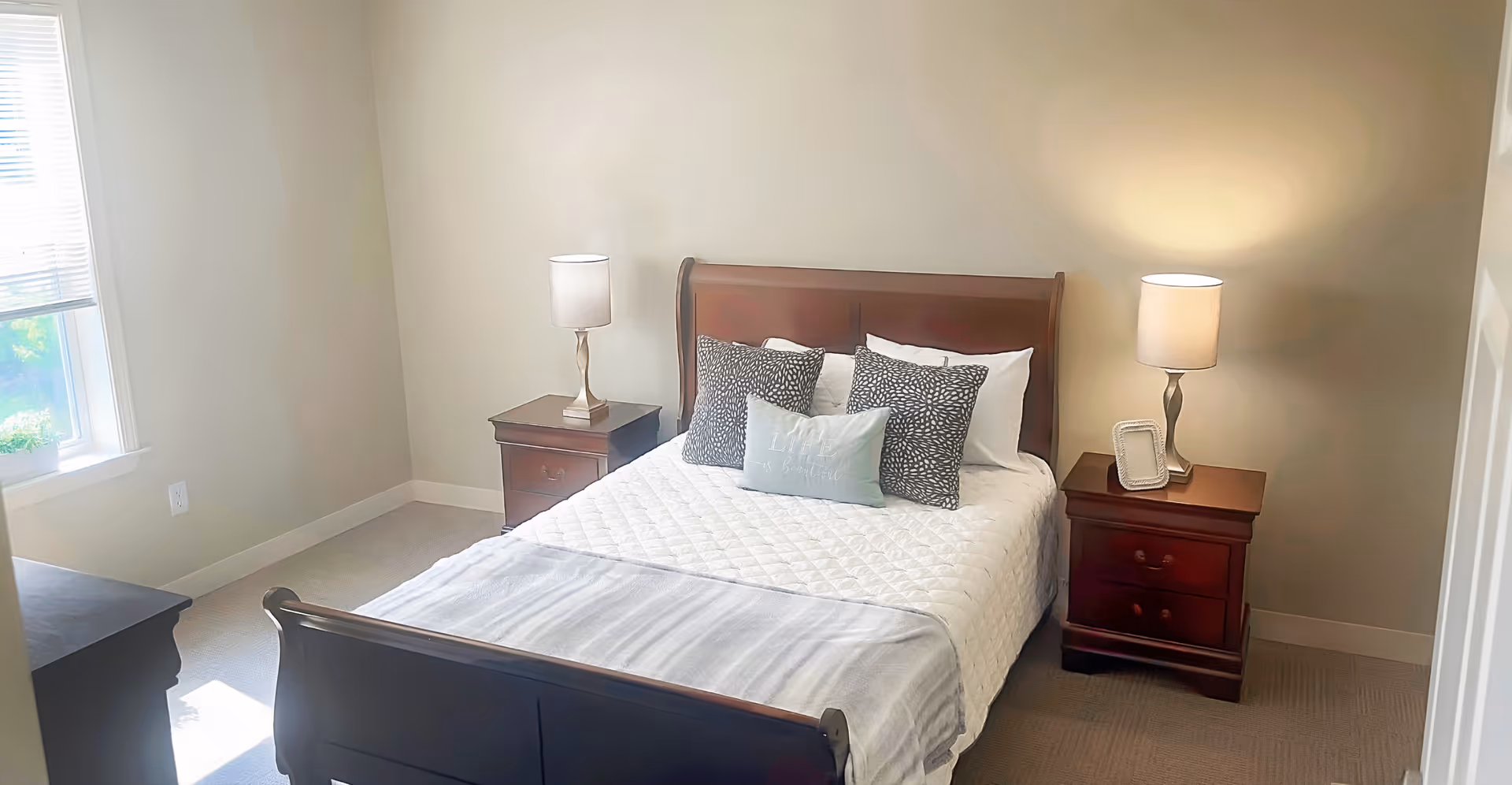Bright bedroom with a wooden sleigh bed, quilted white bedding, decorative pillows, and two nightstands with lamps.