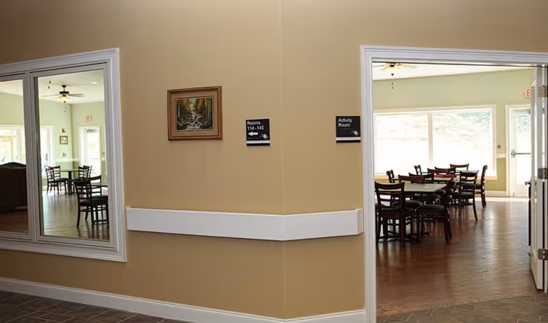 Entrance to a communal activity/dining area with multiple tables and chairs visible through a doorway.