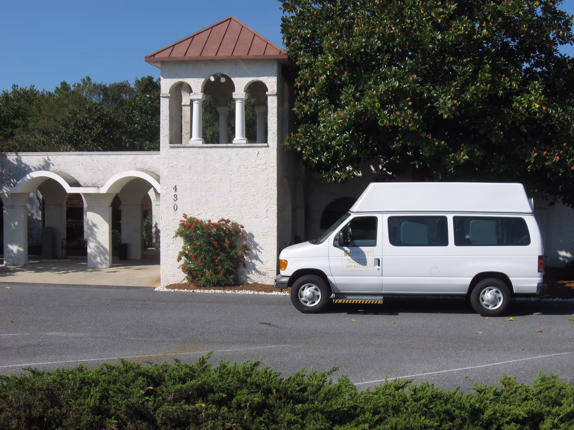 A white passenger van parked outside a white stucco building with arched columns and a small tower.