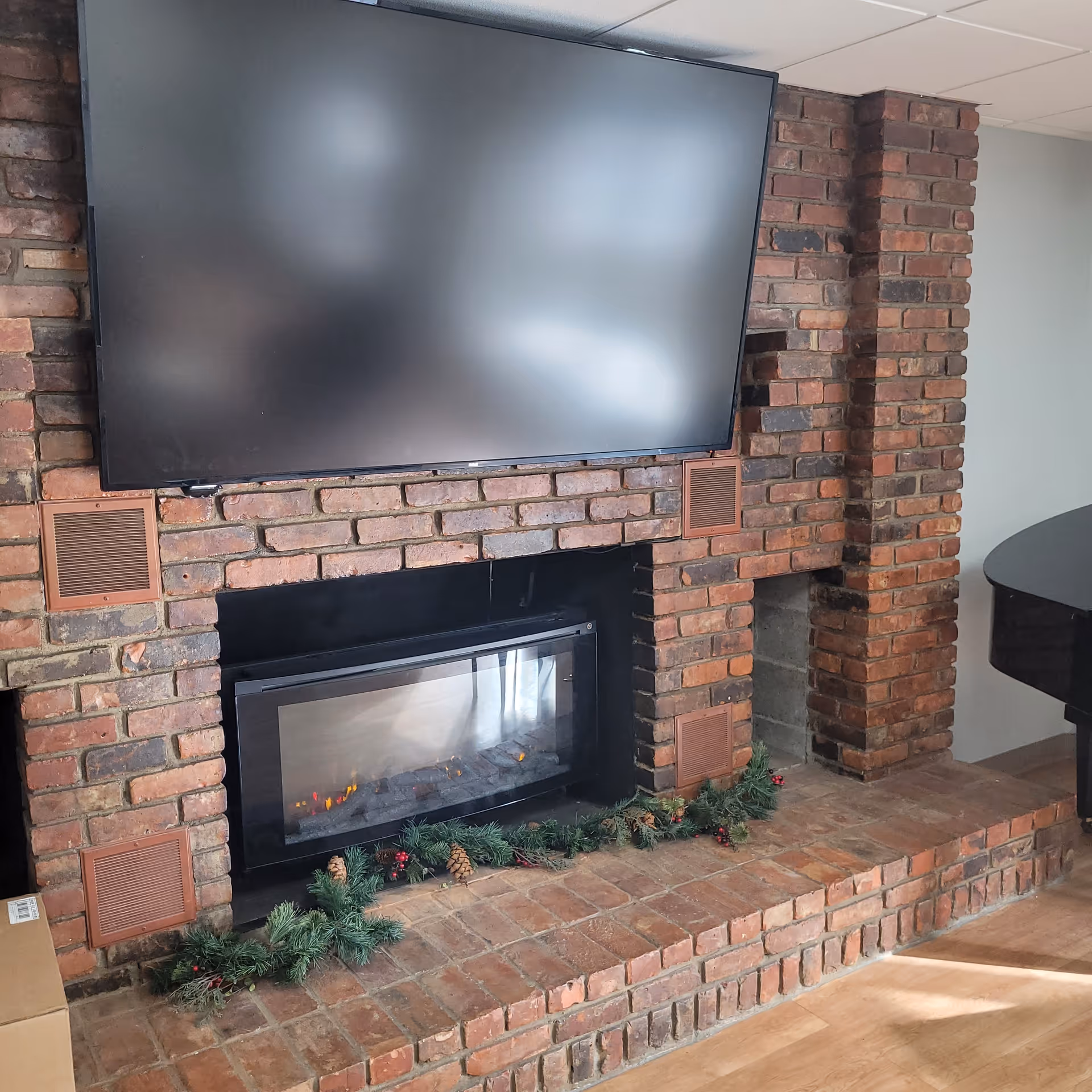 Brick fireplace with a mounted flat-screen TV above, an electric fire insert, and holiday garland on the hearth.