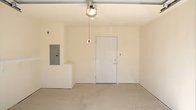 Empty garage interior with a closed side door, utility panel, and overhead garage door opener.
