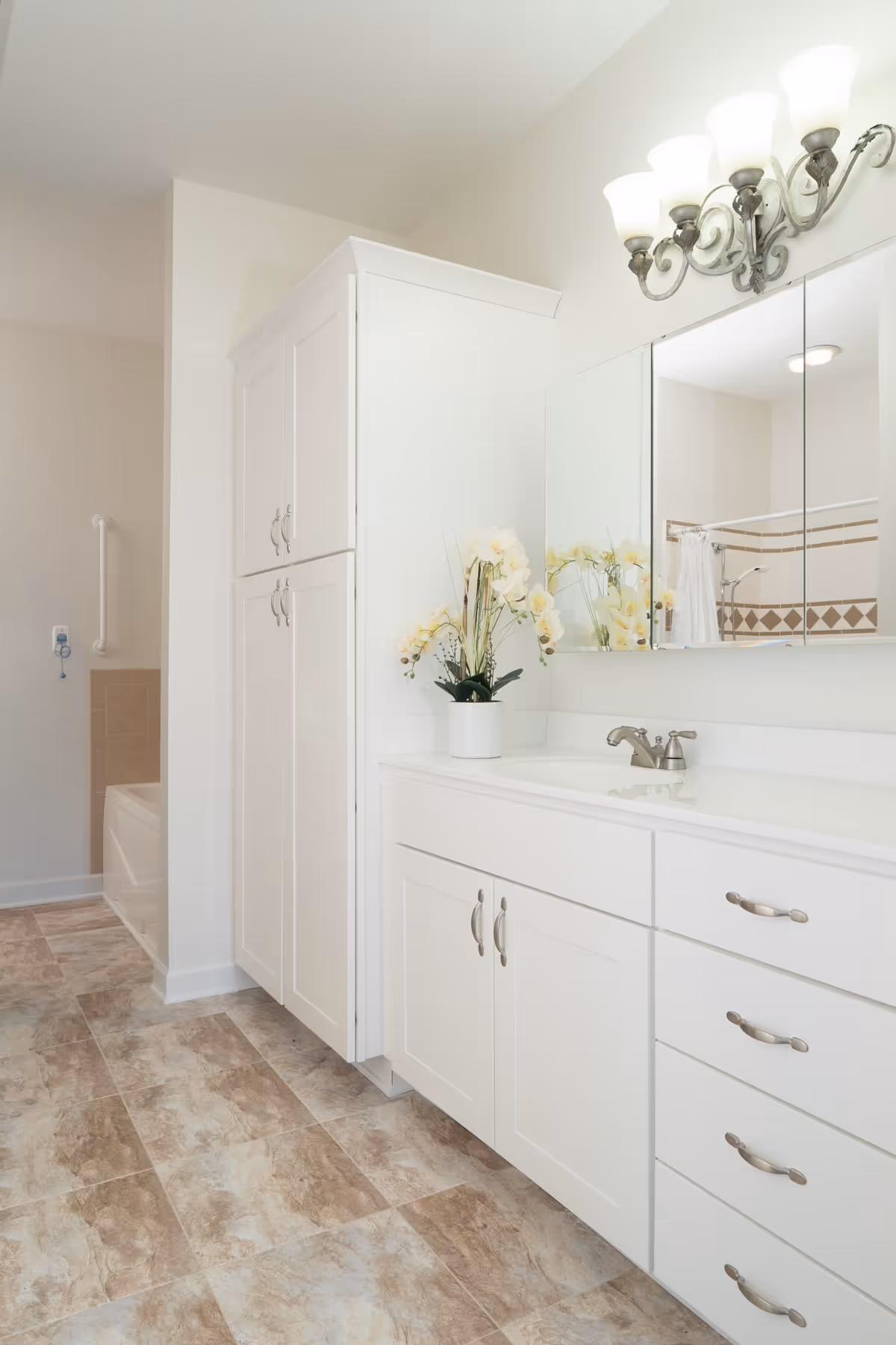 Bright white bathroom featuring a long vanity with sink and mirrored medicine cabinet, tall storage cabinets, and a bathtub with a grab bar.