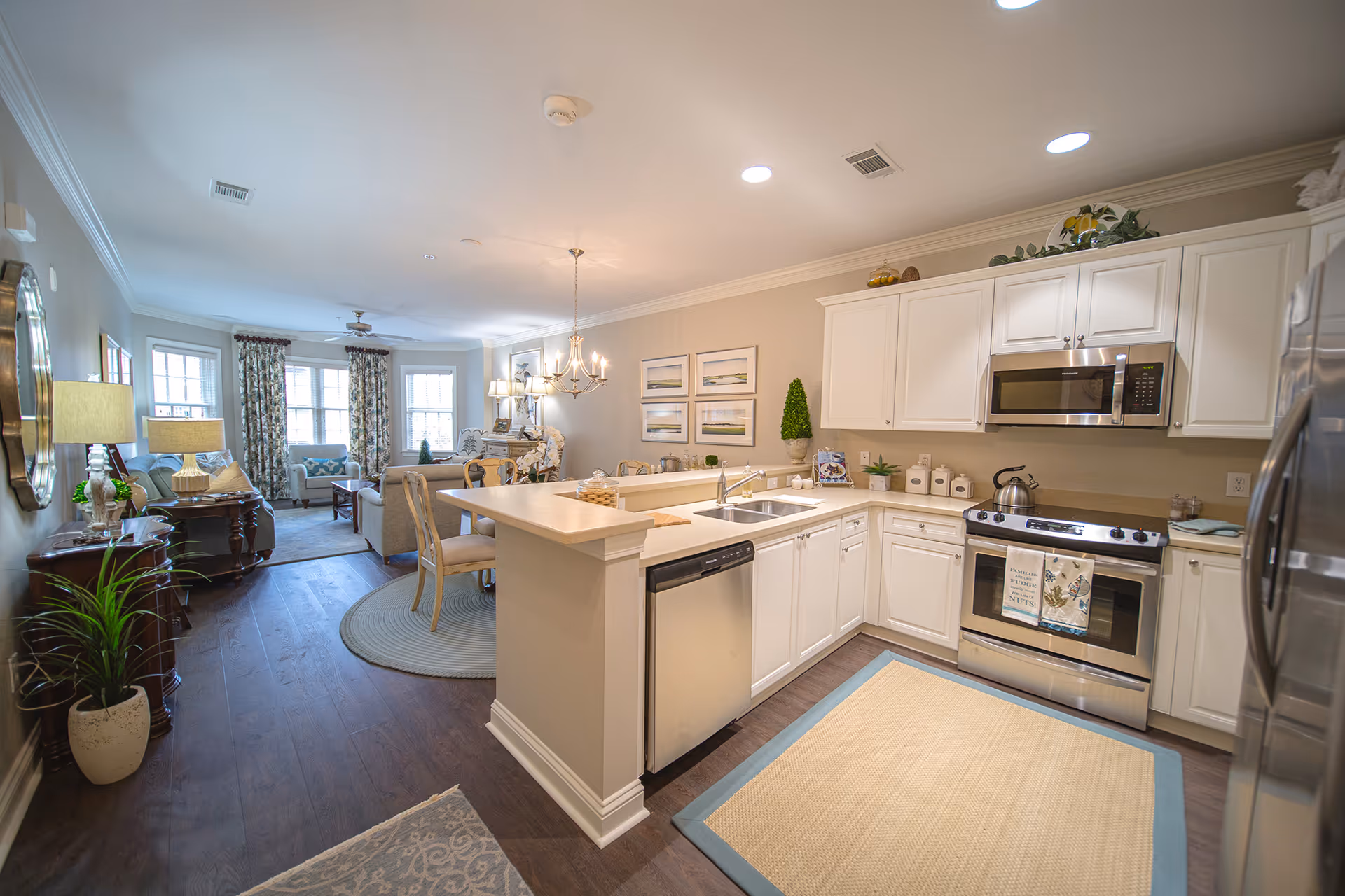 Open-concept kitchen with white cabinets and stainless steel appliances opening into a furnished living and dining area.