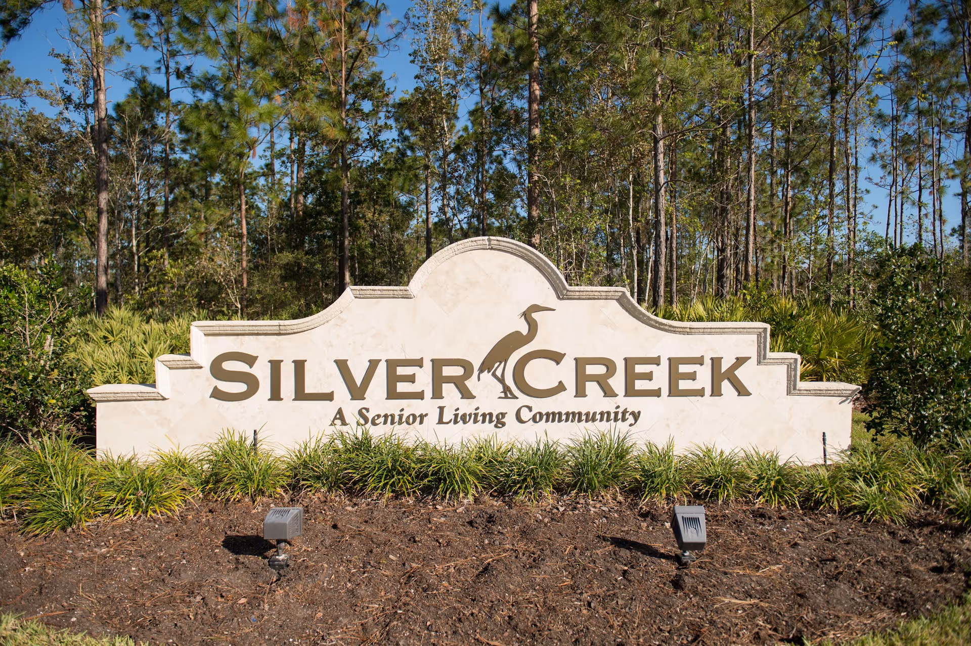 Stone sign for Silver Creek, a senior living community, surrounded by greenery and trees under a clear blue sky.