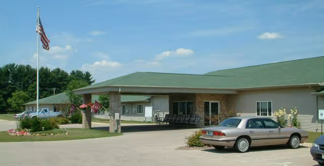 Exterior view of Heartland House senior facility with green roof, flagpole, and parked cars.