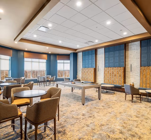Well-lit communal interior with tables, chairs, cushioned benches, and a billiards table.