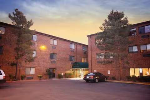 Brick senior living facility exterior at dusk with an entrance and parked cars.