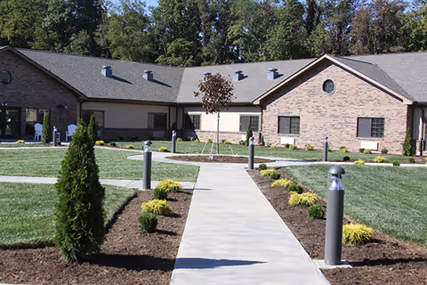 Single-story brick health and rehab building with a central concrete walkway, landscaped lawns, and bollard lights leading to the entrance.