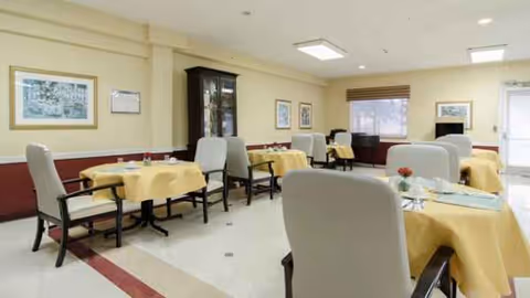 Dining room in a senior facility with yellow tablecloths and beige chairs.