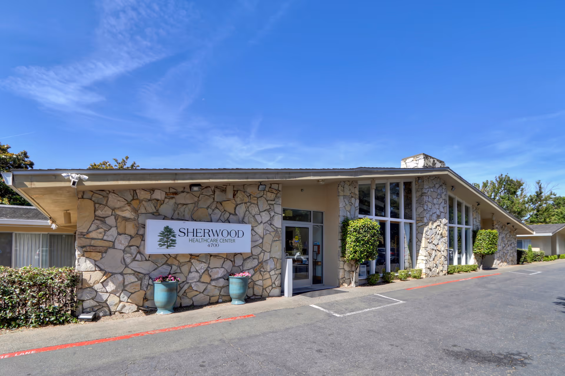 Stone-clad single-story building showing the Sherwood Healthcare Center entrance and sign under a clear blue sky.