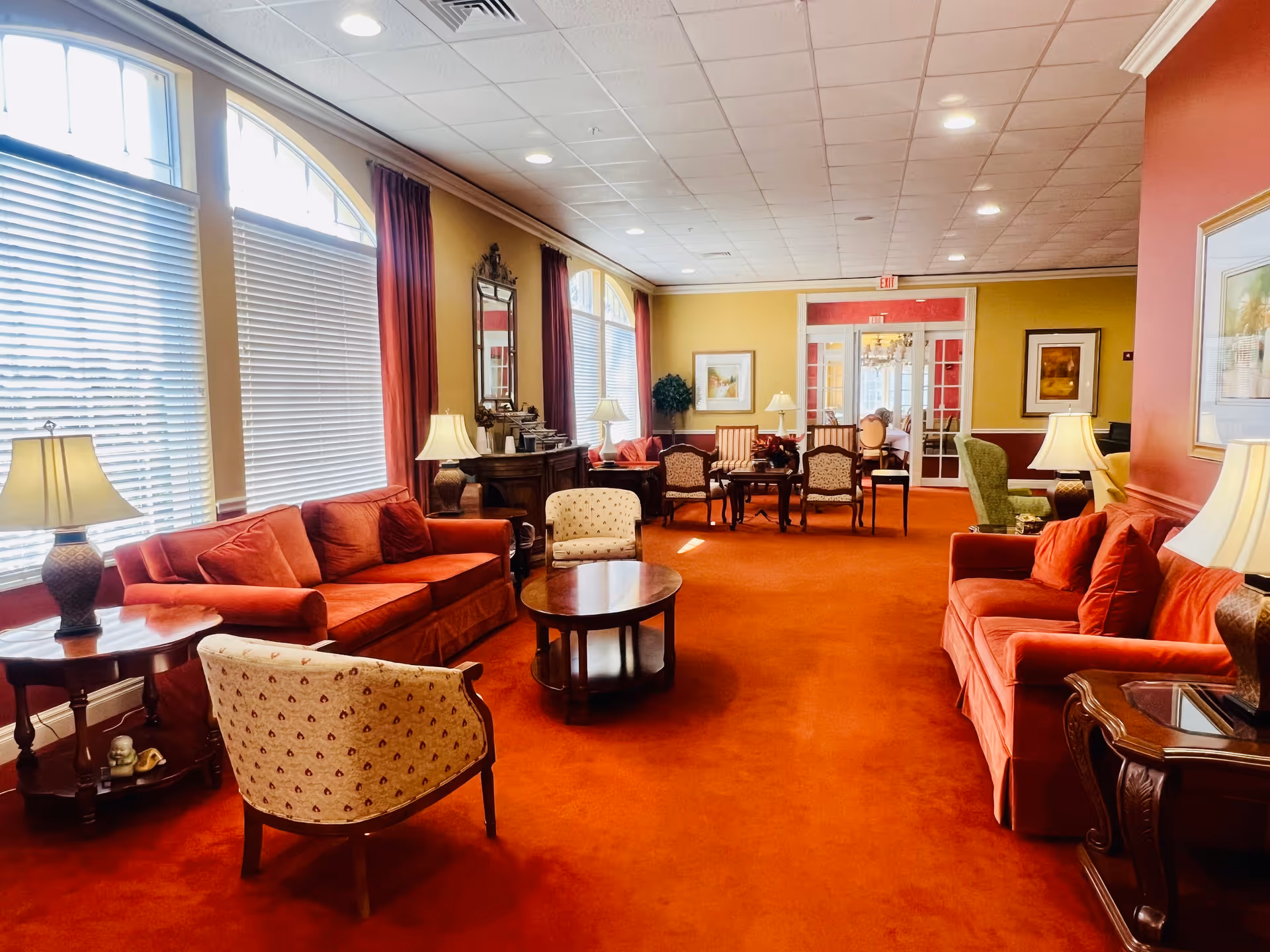 Spacious common lounge with red carpet, sofas, armchairs, coffee tables and large windows.