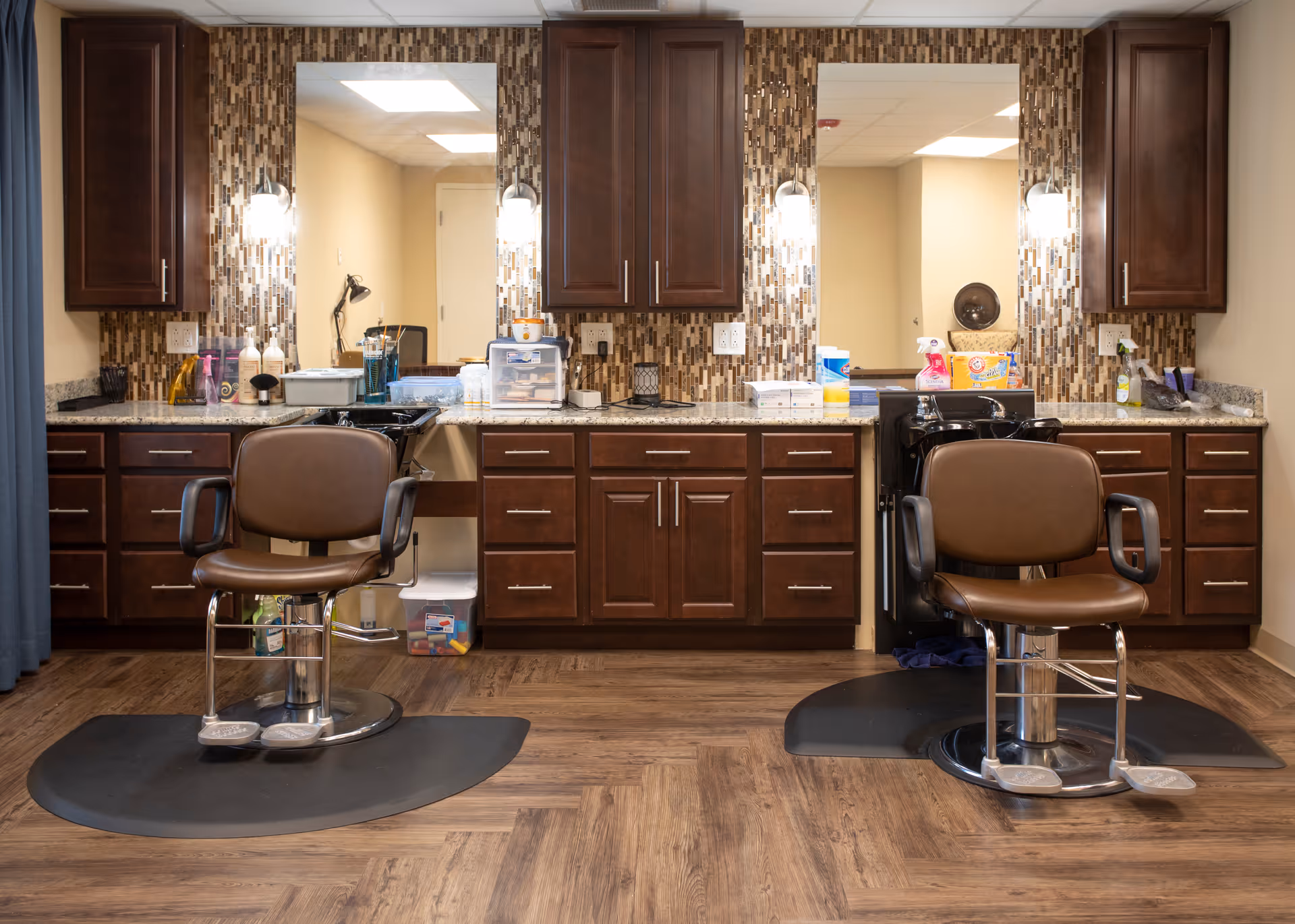 Interior salon area with two barber chairs facing a mirrored countertop and dark wood cabinetry.