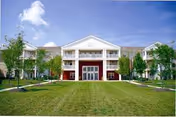 Front exterior view of a two-story senior living facility building named Spring Ridge Senior, with a well-maintained lawn, trees, and a clear blue sky with a few clouds.