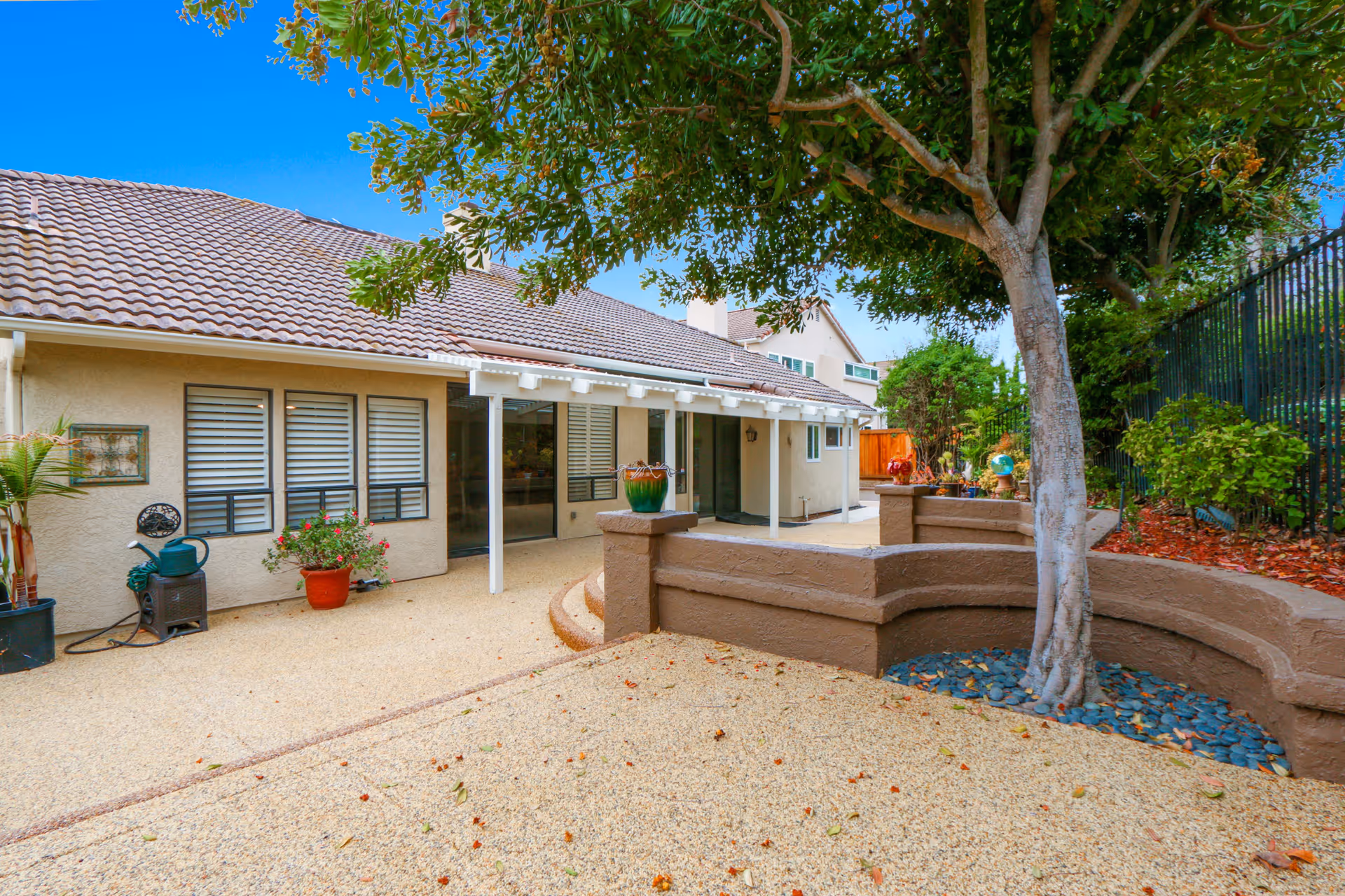 Outdoor patio area with a covered walkway, raised planter walls, a large tree, and the building exterior.