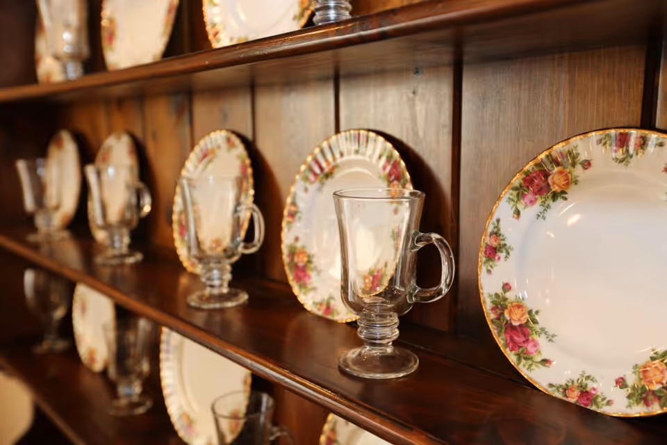 Wooden hutch shelf displaying floral china plates and clear glass mugs.