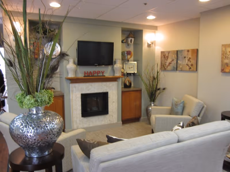 Cozy living-room lounge with sofas and armchairs arranged around a fireplace and wall-mounted TV, decorated with large vases and artwork.