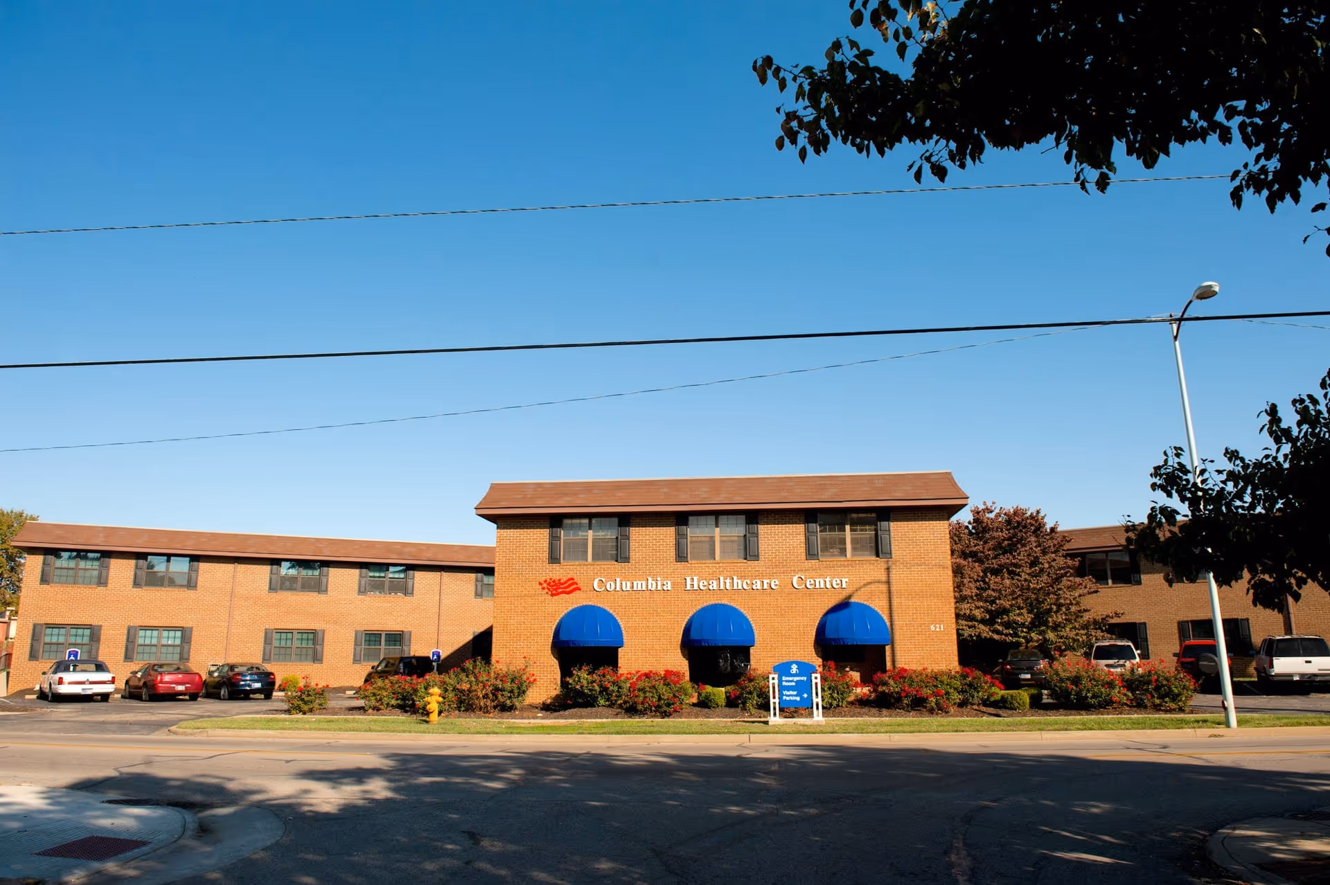 Front exterior of a two-story brick building labeled Columbia Healthcare Center with three blue awnings and a small parking lot.
