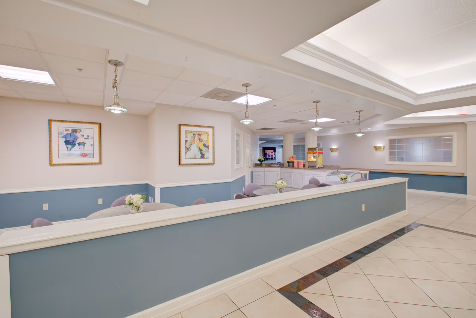 Well-lit common area with tables, chairs, pendant lights, framed art, and a service counter.