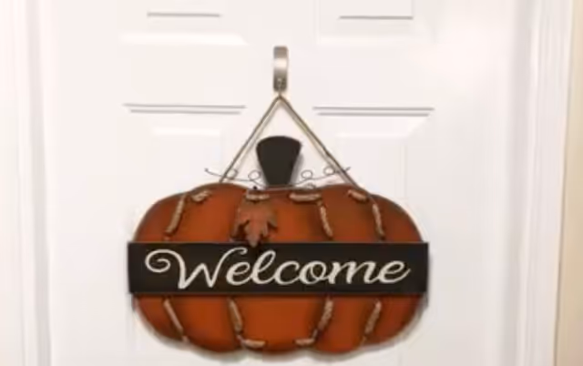 A pumpkin-shaped 'Welcome' door sign hanging on a white door.